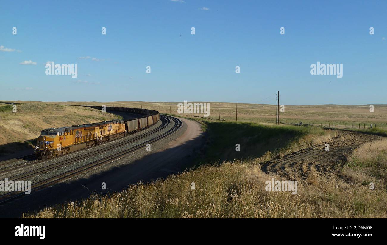 Lungo treno di carbone che circonda una curva nel bacino rurale del fiume Powder del Wyoming. Foto Stock