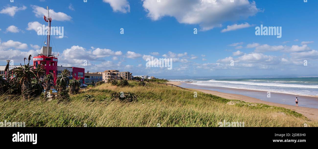 Edifici fronte spiaggia e una persona in piedi sulla riva guardando l'oceano fare surf lungo Dolphin Beach a Jeffrey's Bay; Eastern Cape, Sud Africa Foto Stock