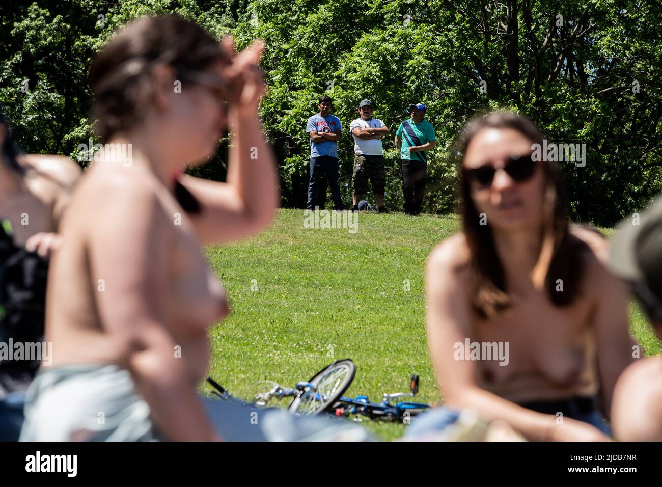 I manifestanti topless giacciono sull'erba, mentre un gruppo di uomini guarda la protesta da lontano. Foto Stock