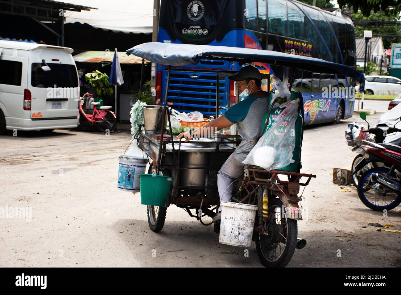 Uomini thailandesi si siedono e cavalcano in moto con carrello triciclo per cucinare e vendere Instant e tagliatelle sulla strada di vicolo piccolo a Bang Bua Tho Foto Stock