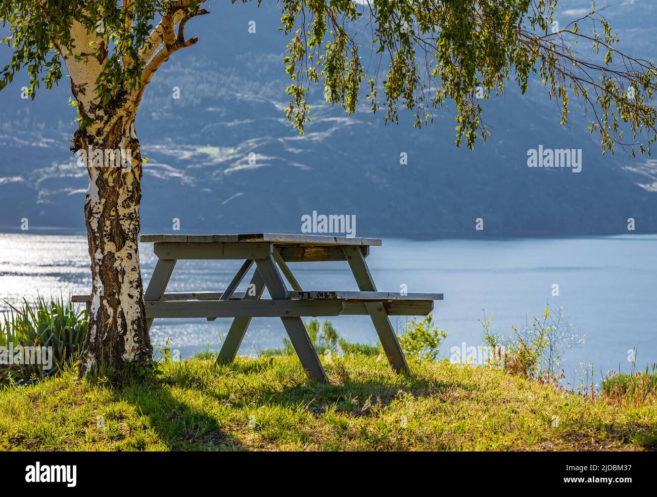Tavolo vuoto in legno con sedie sulla collina di un parco estivo al lago Okanagan BC Canada. Giornata calda di sole vicino al lago. Paesaggio alba mattina. Tra Foto Stock