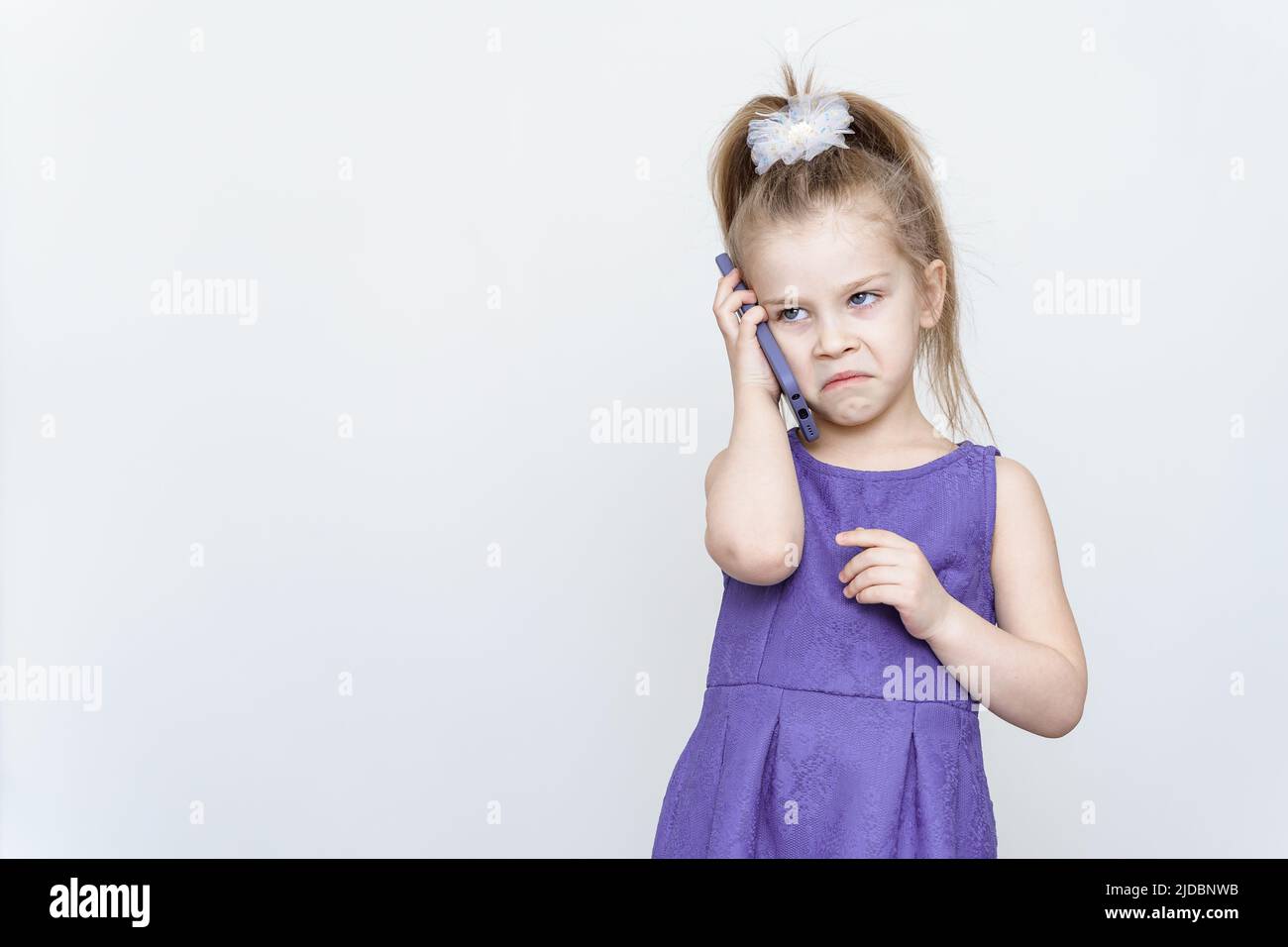 bambina arrabbiata in abito blu che parla al telefono Foto Stock