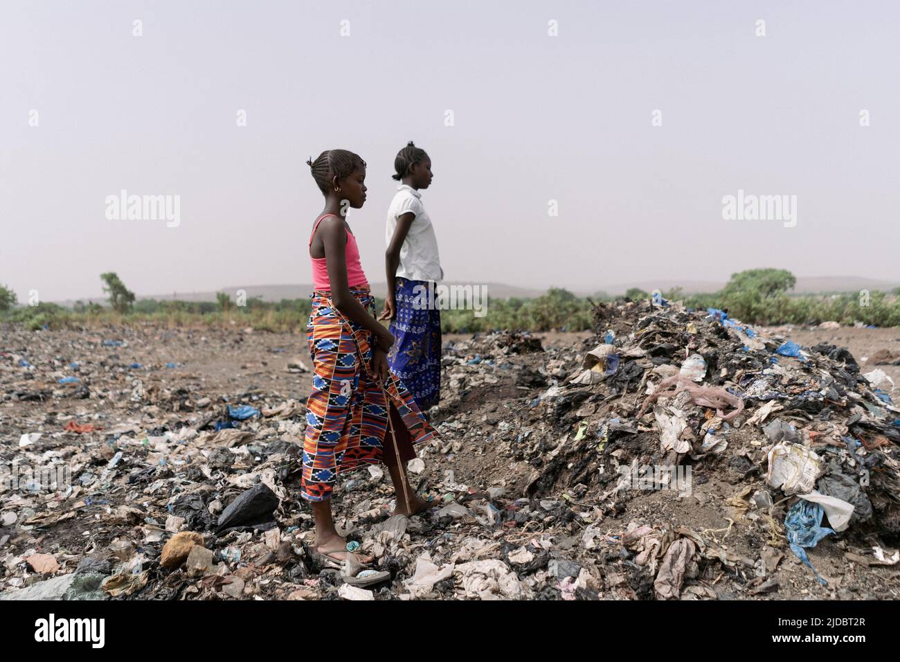 Due ragazze africane del colletter della spazzatura che prendono una rottura che si levano in piedi diritto per riposare la loro parte posteriore dolorante mentre cercano il materiale riciclabile in una discarica Foto Stock