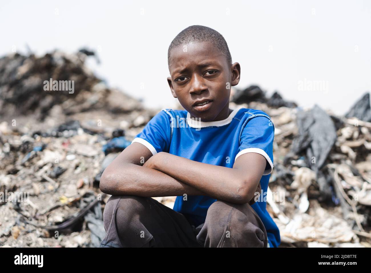 Giovane raccolta di rifiuti africani seduta stanca su un mucchio di rifiuti di plastica in una discarica che contempla l'ambiente brutto; concetto di povertà, c Foto Stock