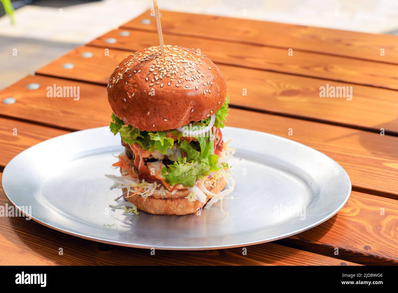 Hamburger alto grande e gustoso o hamburger di manzo con verdure e salsa su piatto di metallo su tavola di legno. Brunch in giornata di sole. Primo piano, spazio copia, avanti Foto Stock