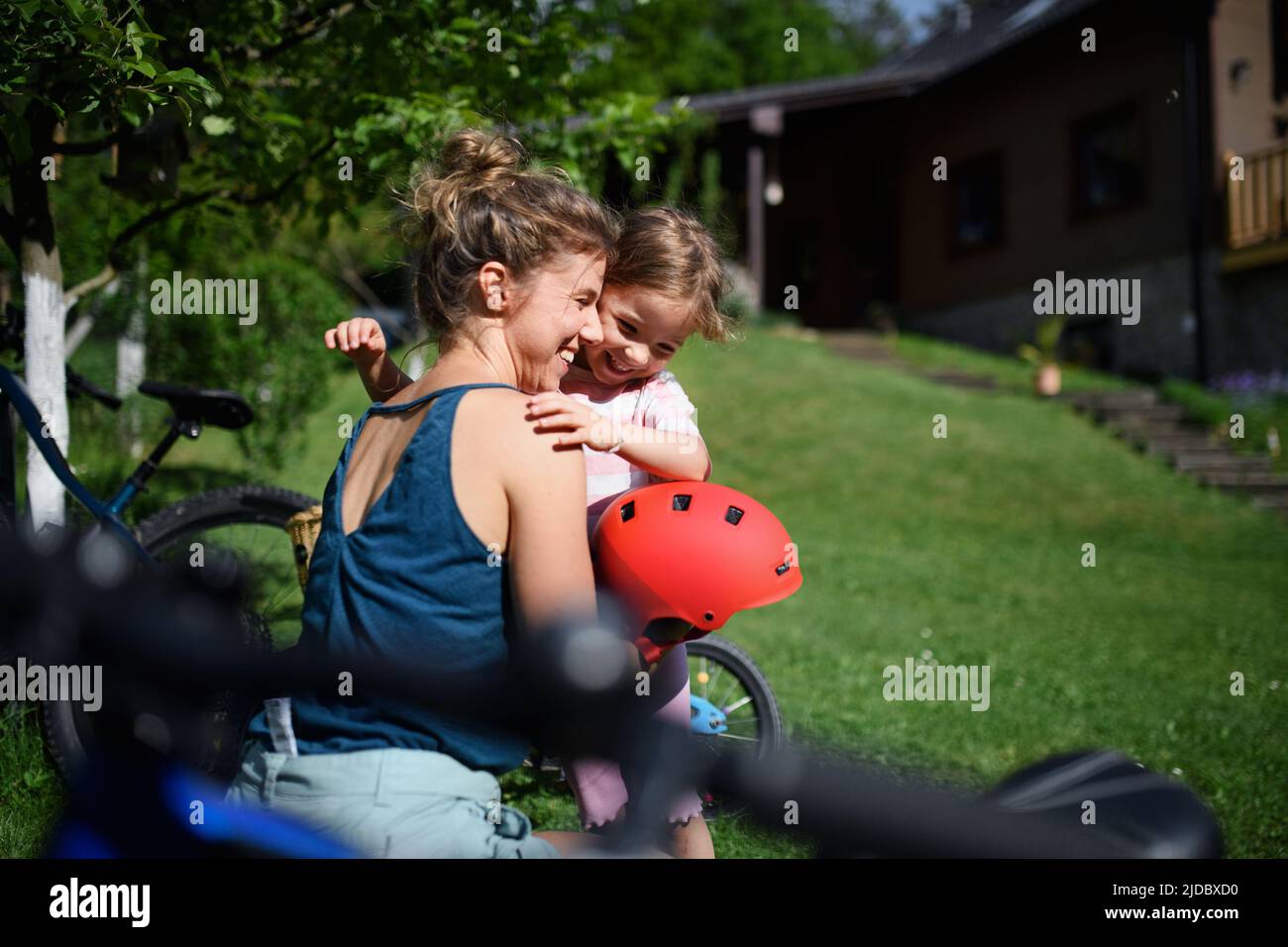 Giovane madre con bambina preaparing per il giro in bicicletta, mettendo i caschi. Foto Stock