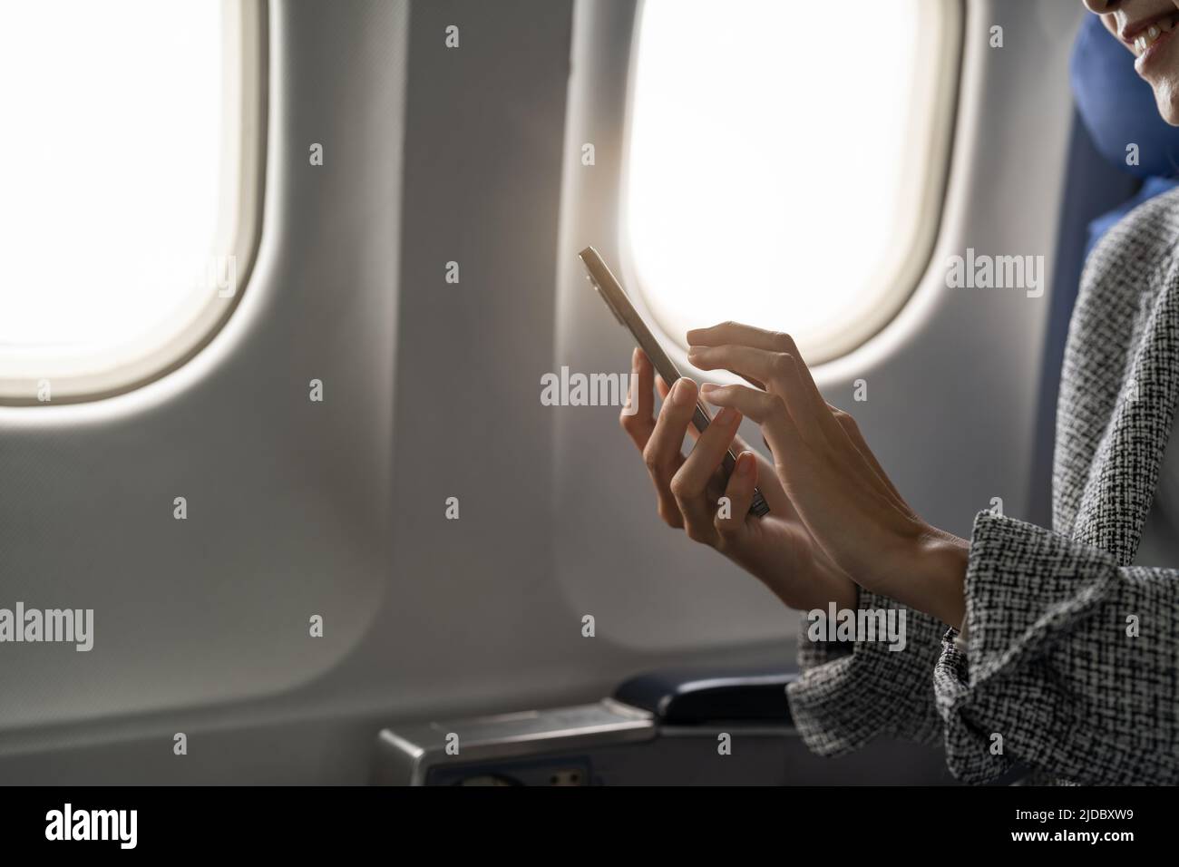 Vista laterale di una giovane donna d'affari che utilizza lo smartphone in aereo, un hipster che tiene un dispositivo mobile per giocare o lavorare durante il volo, viaggi d'affari Foto Stock