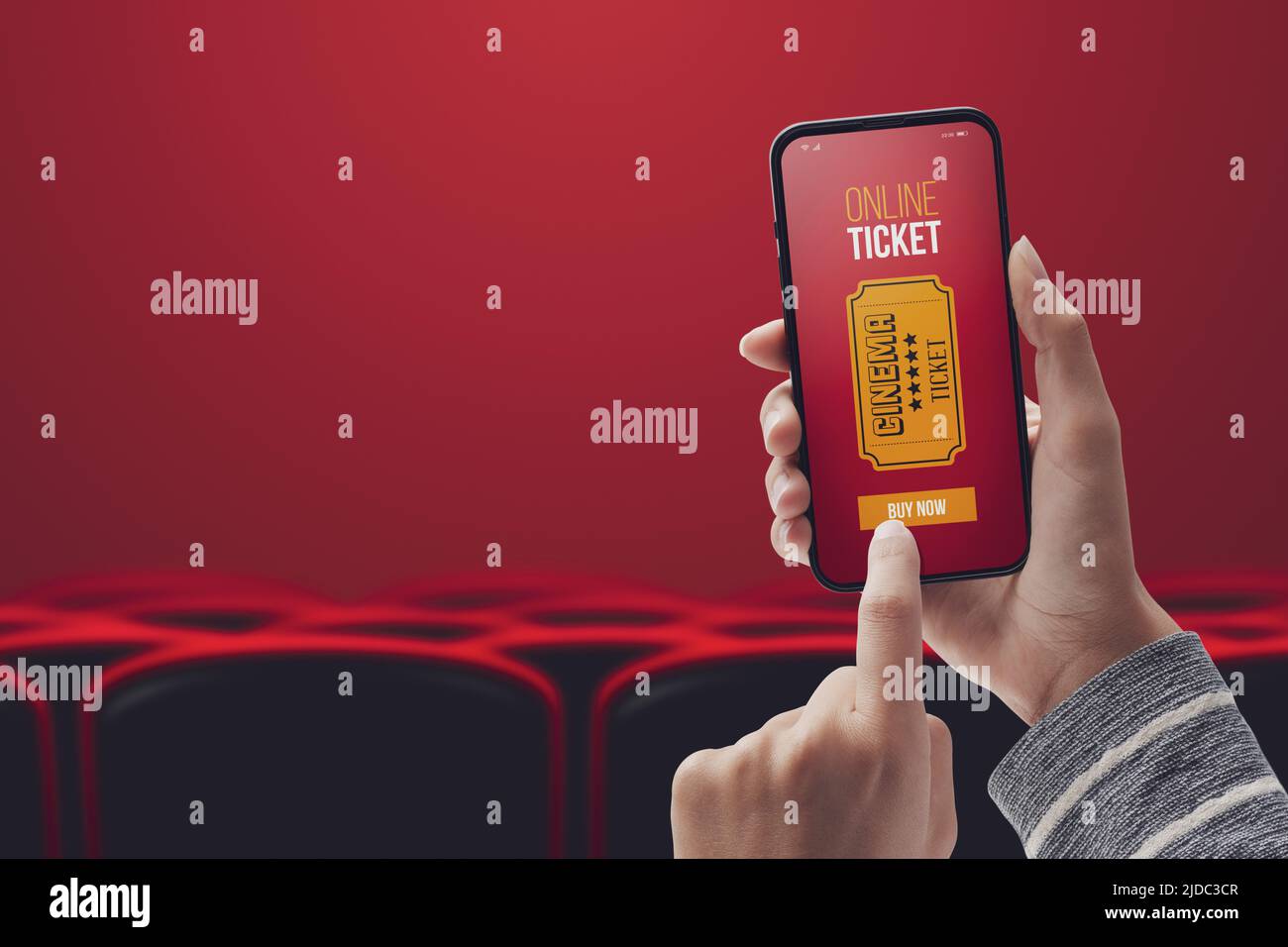 Donna che tiene uno smartphone e acquista biglietti per film online utilizzando un'app mobile, una sala cinema e posti a sedere in background, ripresa POV Foto Stock
