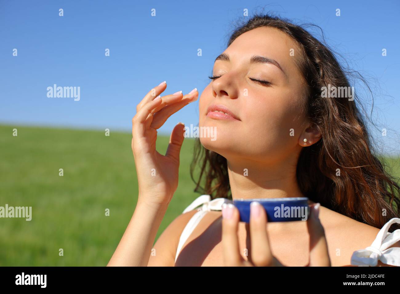 Donna che applica crema moisturizer nel suo viso in un campo una giornata di sole Foto Stock