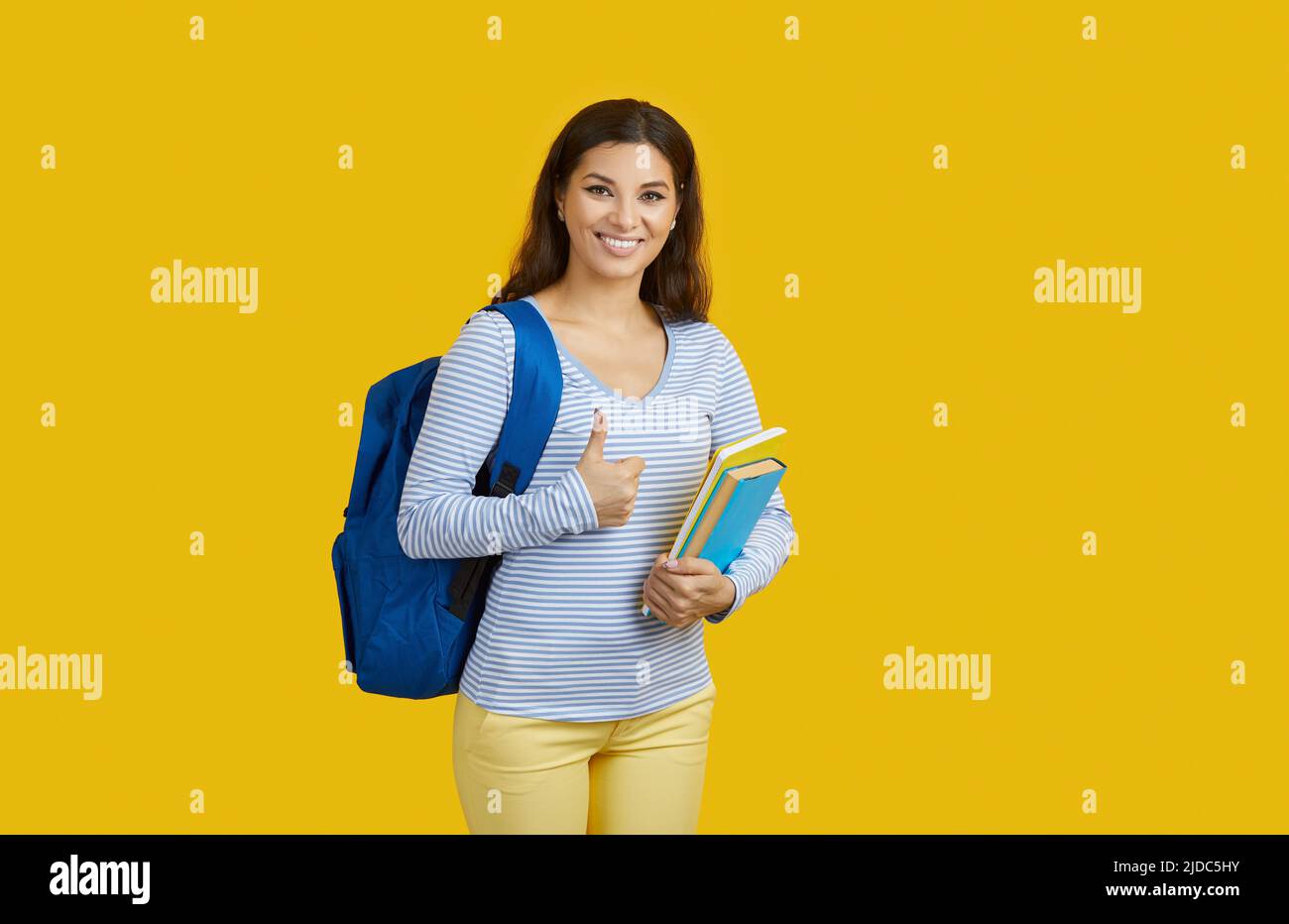 Scuola elementare con zaino che mostra il pollice in su e sorridendo su sfondo giallo vibrante, concetto di istruzione. Foto Stock