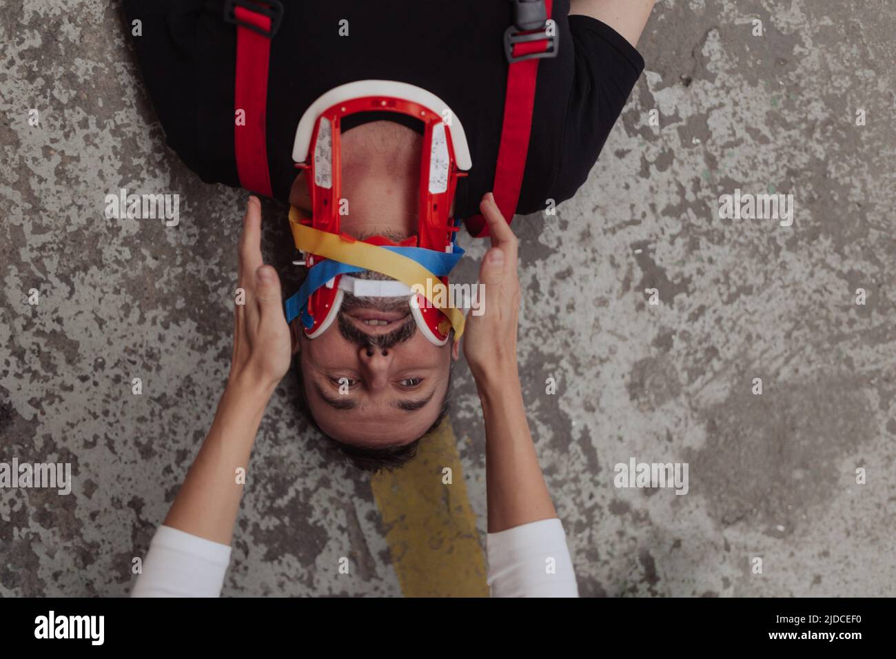 Vista dall'alto mani paramediche che si prendono cura del paziente dopo un incidente di lavoro in una caffetteria, fissando la testa dell'uomo. Foto Stock