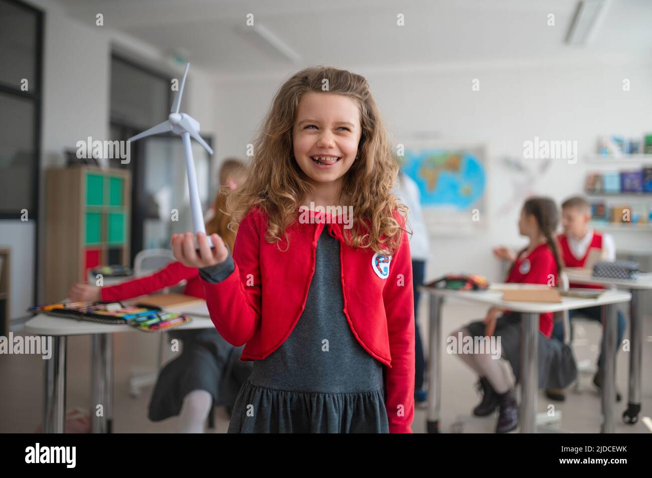 Studentessa che tiene la turbina eolica e che impara a conoscere le fonti di energia rinnovabili ecocompatibili in classe a scuola Foto Stock