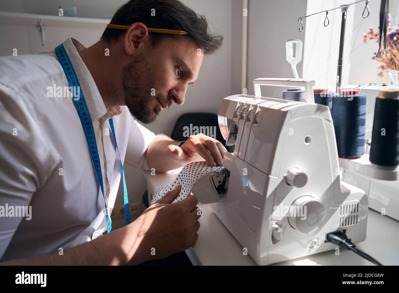 Uomo che si gode di fare i vestiti in atelier con attrezzature moderne Foto Stock