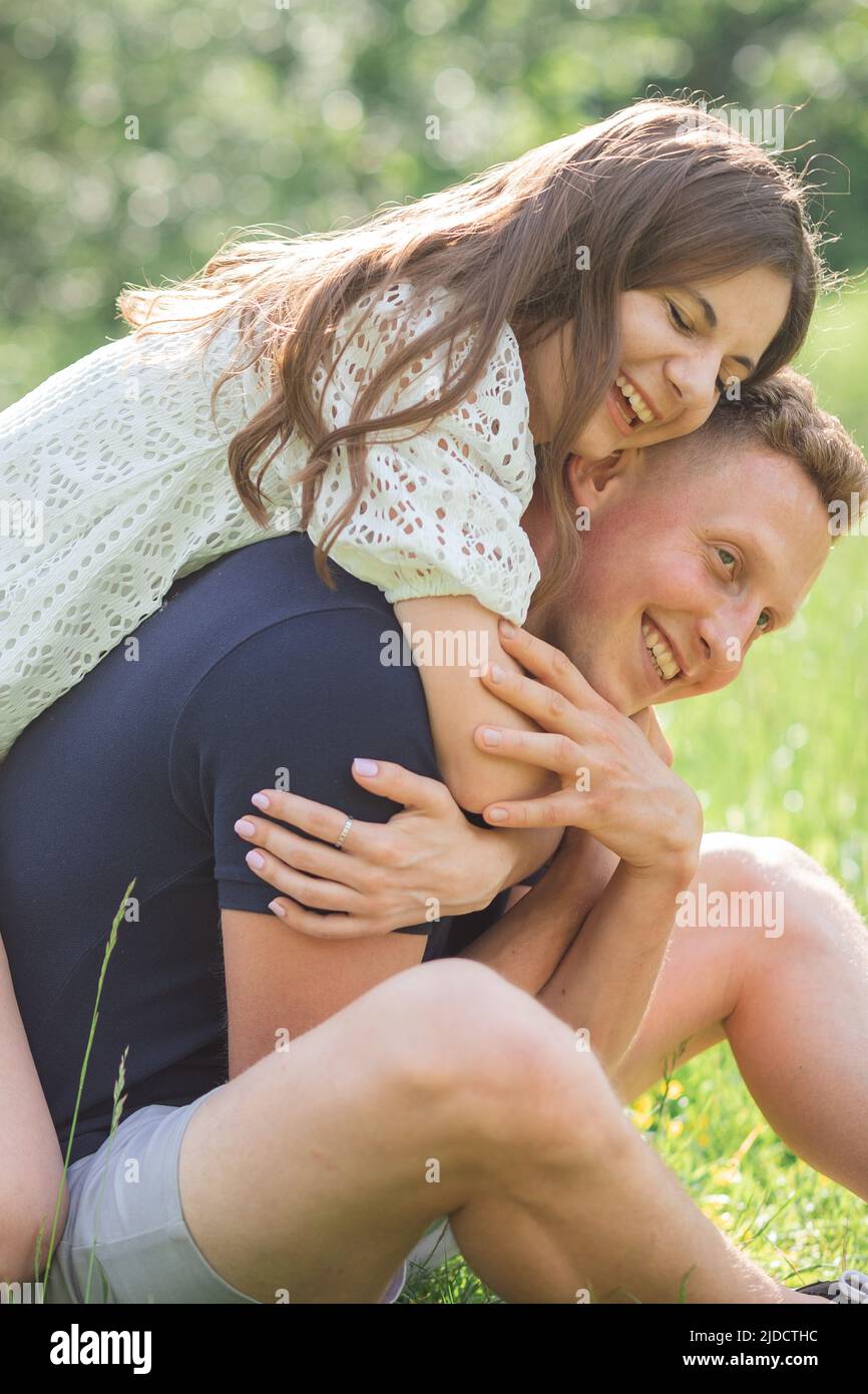 Giovane coppia affettuosa seduta sull'erba nel parco, guardando l'un l'altro. Giovane uomo e donna che si godono giorno d'estate. Gente felice nell'amore, luna di miele Foto Stock