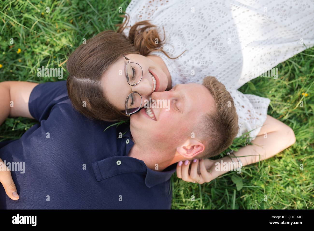 Divertimento estivo di uomo e donna. Vista dall'alto della giovane coppia innamorata adagiata sull'erba e sorridente, luna di miele, gente felice Foto Stock