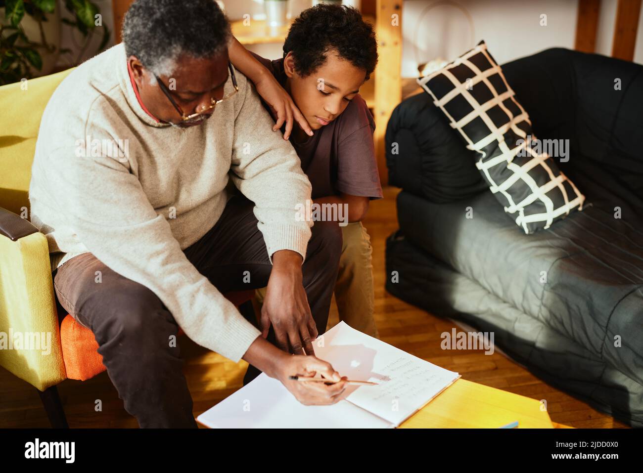 Un nonno afroamericano è seduto a casa con il nipote e gli spiega un problema di matematica. Foto Stock