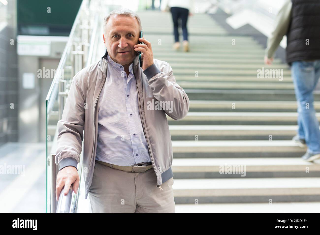 Uomo di mezza età con telefono che scende le scale nel centro commerciale Foto Stock
