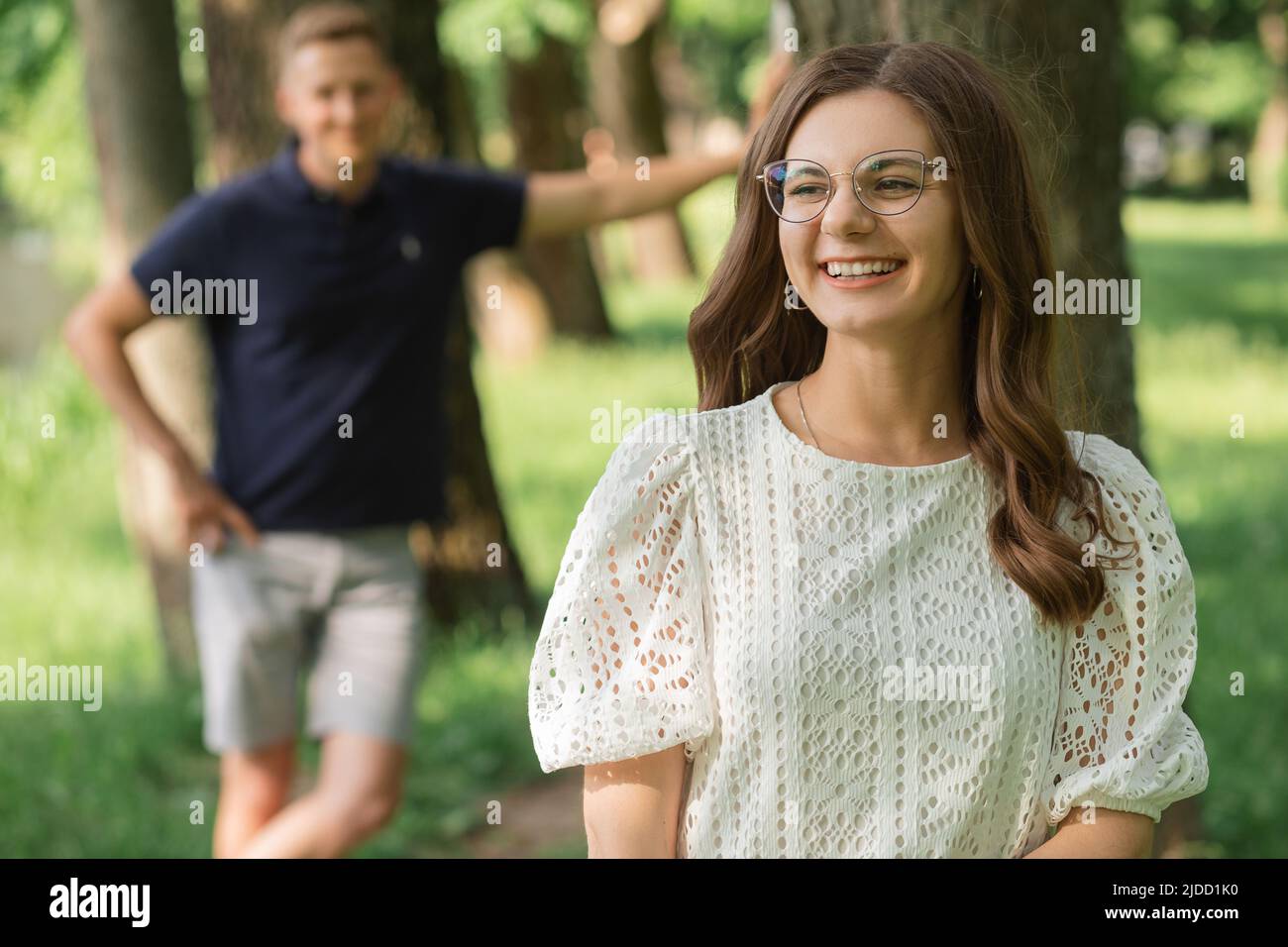 l'uomo defocused fuoco sulla donna sorridente nel parco fra gli alberi, la gente felice che ha divertimento il giorno d'estate, la coppia nell'amore. Foto Stock