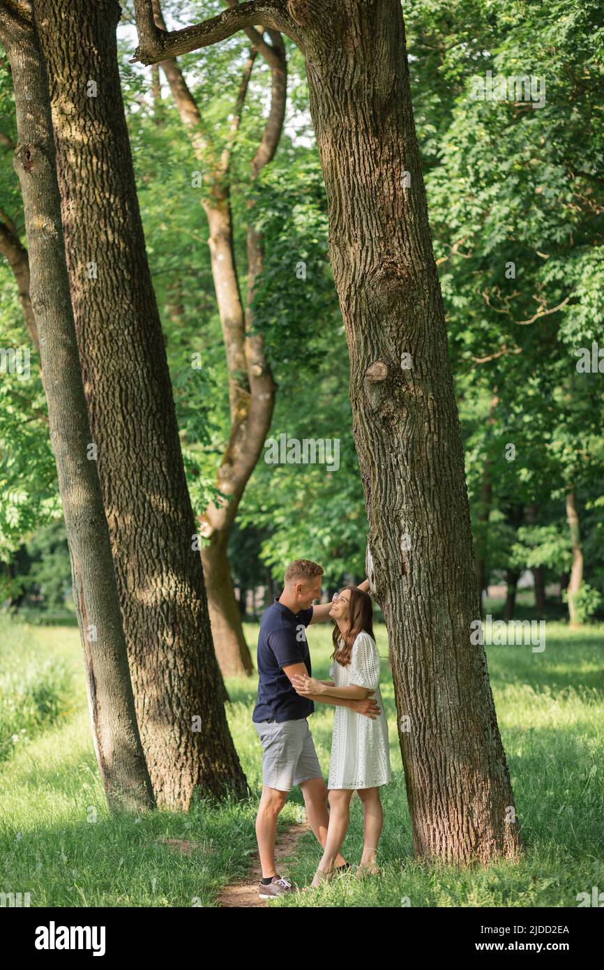 tutta la lunghezza di giovane coppia felice in estate in piedi vicino al lago, abbracciando, gente felice nel parco fra gli alberi grandi, Foto Stock