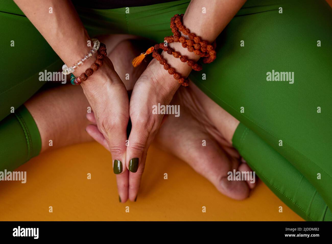 Primo piano di una donna yoga seduta sul tappeto yoga a casa in una posa di loto e meditating. Sta tenendo le mani in ksepana mudra. Foto Stock