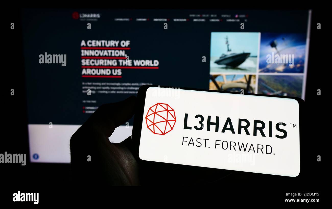 Persona che tiene il cellulare con il logo della società aerospaziale americana L3Harris Technologies Inc. Sullo schermo di fronte alla pagina web. Mettere a fuoco sul display del telefono. Foto Stock