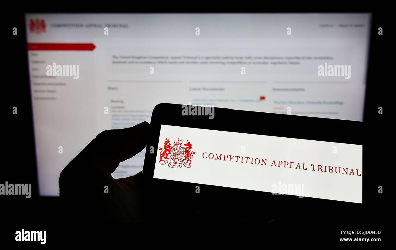 Persona che tiene il cellulare con il logo del British Body Competition Appeal Tribunal (CAT) sullo schermo di fronte alla pagina web. Mettere a fuoco sul display del telefono. Foto Stock