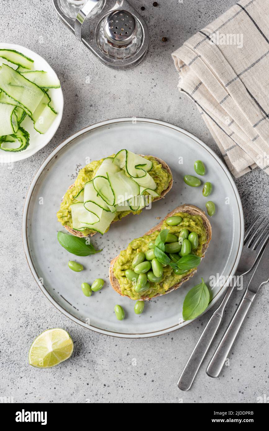 Toast di avocado verde sano con fagioli e cetrioli su un piatto, vista da tavolo. Concetto di consumo pulito Foto Stock