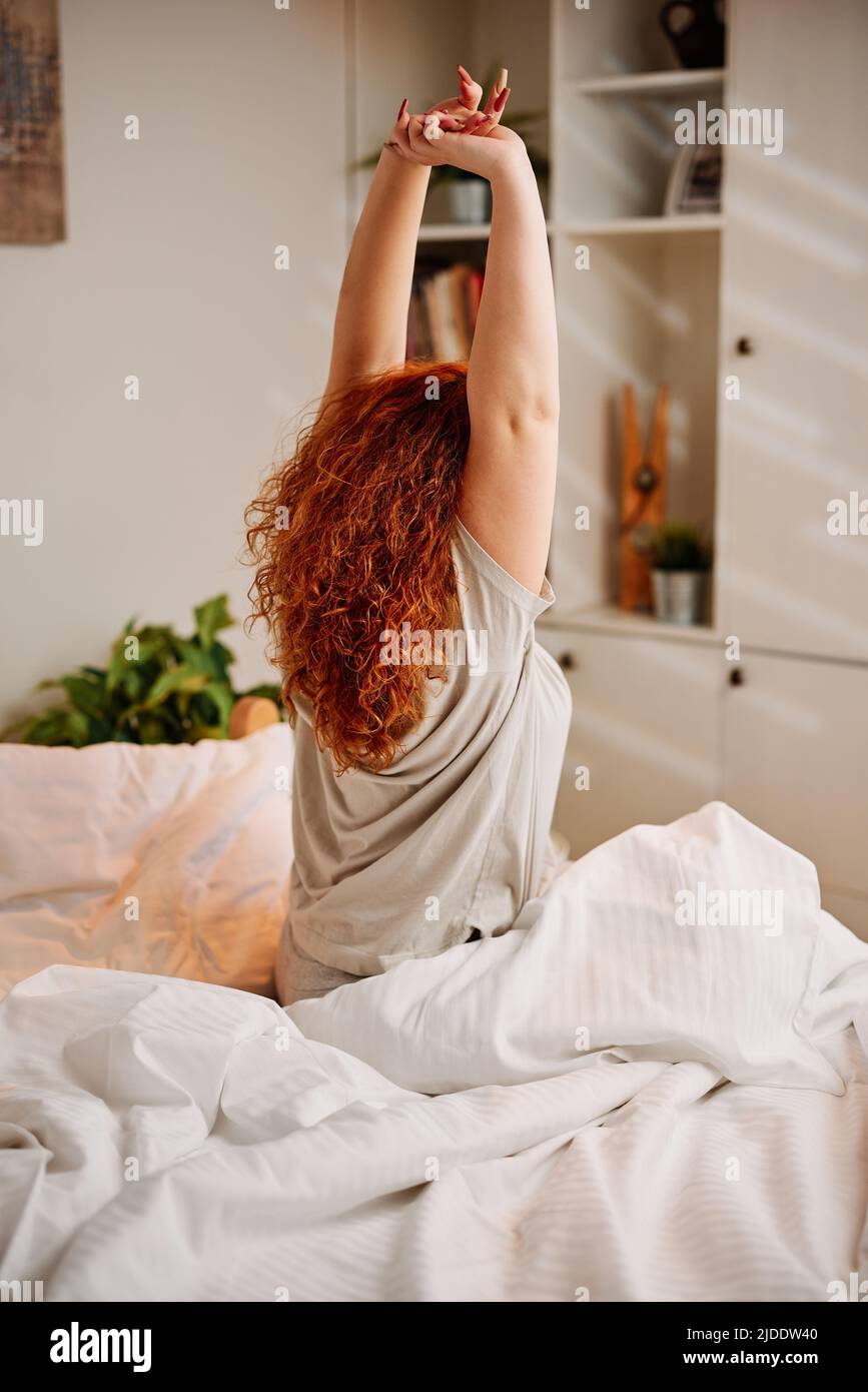 Una ragazza rossa si sveglia al mattino e allunga le braccia. Foto Stock