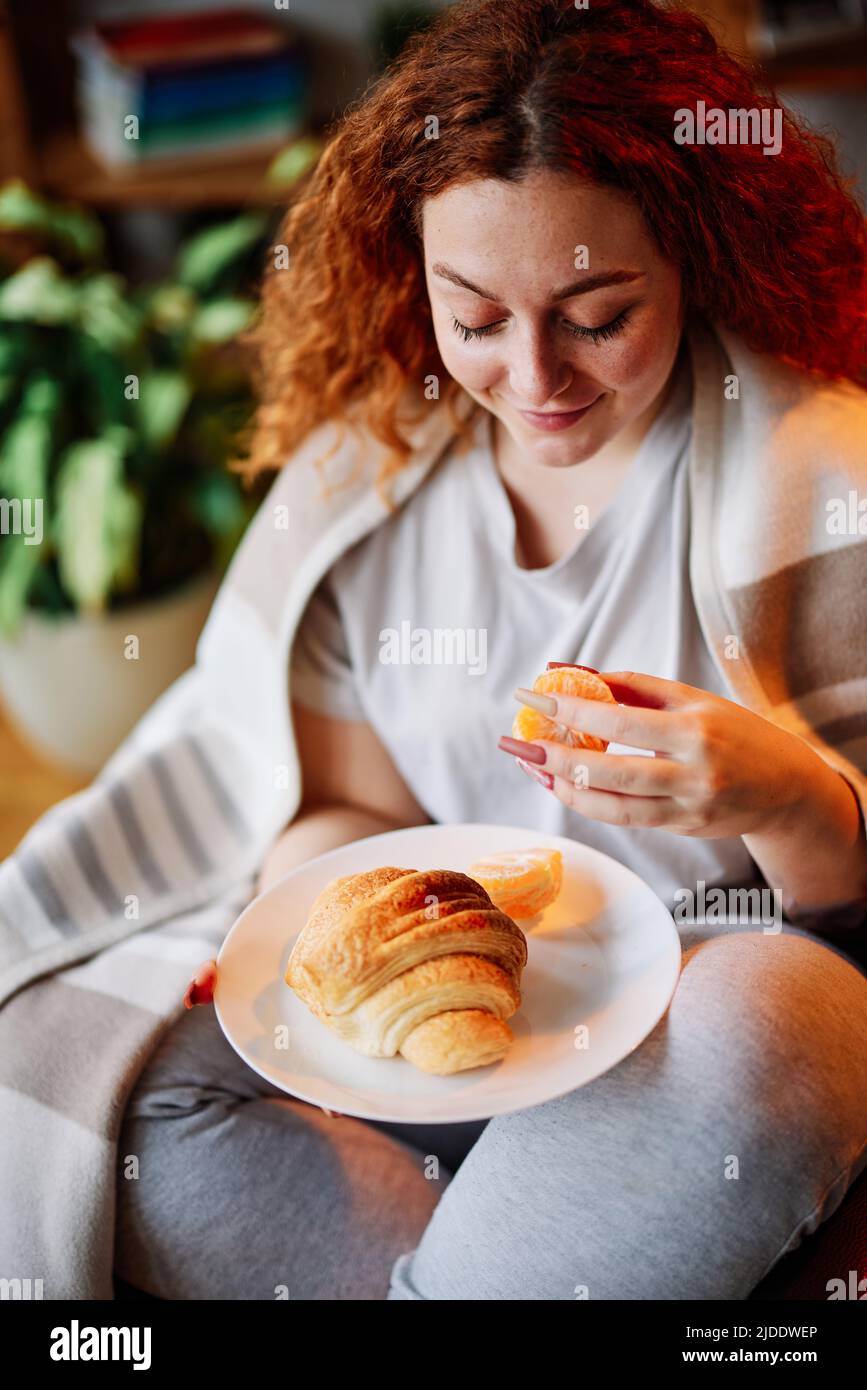 Una rossa affamata seduta nella sua casa accogliente al mattino e fare colazione. Foto Stock