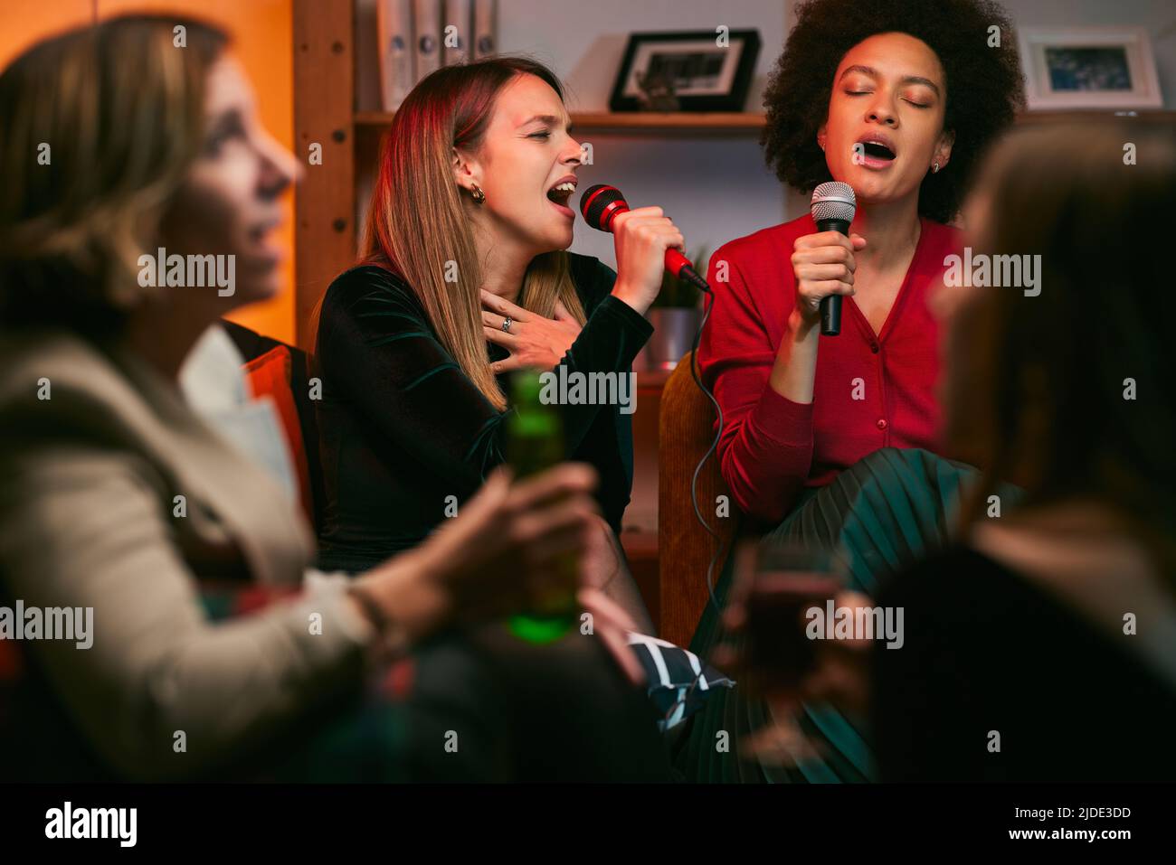 Amici multirazziali di talento si siedono a casa e cantano un duetto a casa nella notte del karaoke. Foto Stock