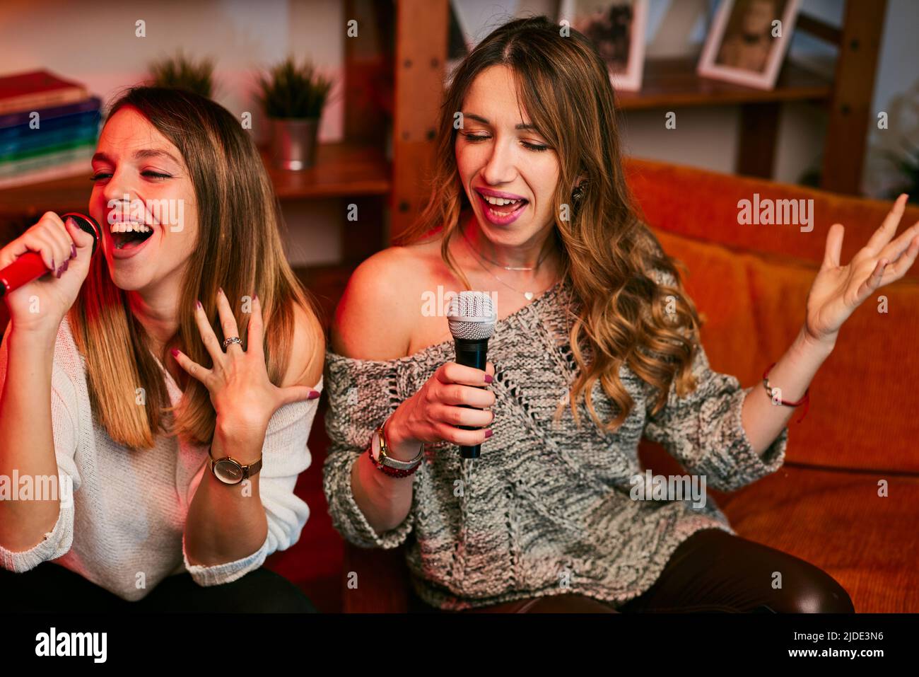 Ragazze di talento con belle voci si siedono a casa e cantano un duetto alla notte del karaoke. Foto Stock