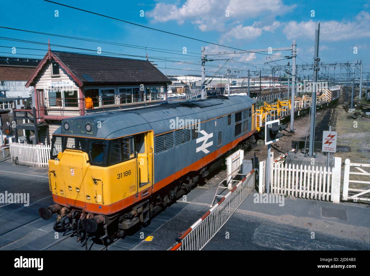 Una locomotiva diesel di classe 31 numero 31186 con il treno di manutenzione della linea aerea supera la cassa di segnalazione e l'attraversamento del livello a Dagenham Dock il 8th luglio 1990. Foto Stock