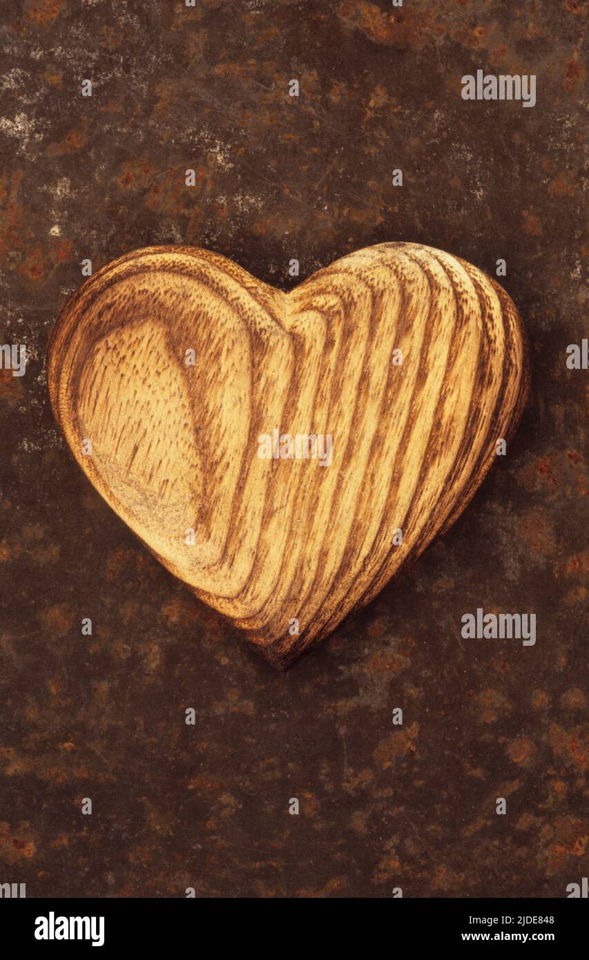 Primo piano dall'alto della forma del cuore di legno intagliato per mostrare gli anelli dell'albero e il grano di legno che giace su foglio di metallo arrugginito Foto Stock