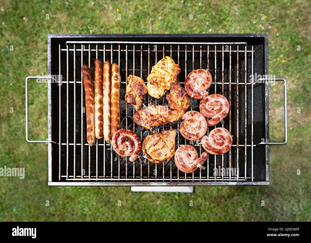 Gustoso assortimento di carne su un barbecue estivo con bistecche, pollo, salsicce, salsicce di manzo spirali. Vista dall'alto sull'erba verde. Foto Stock