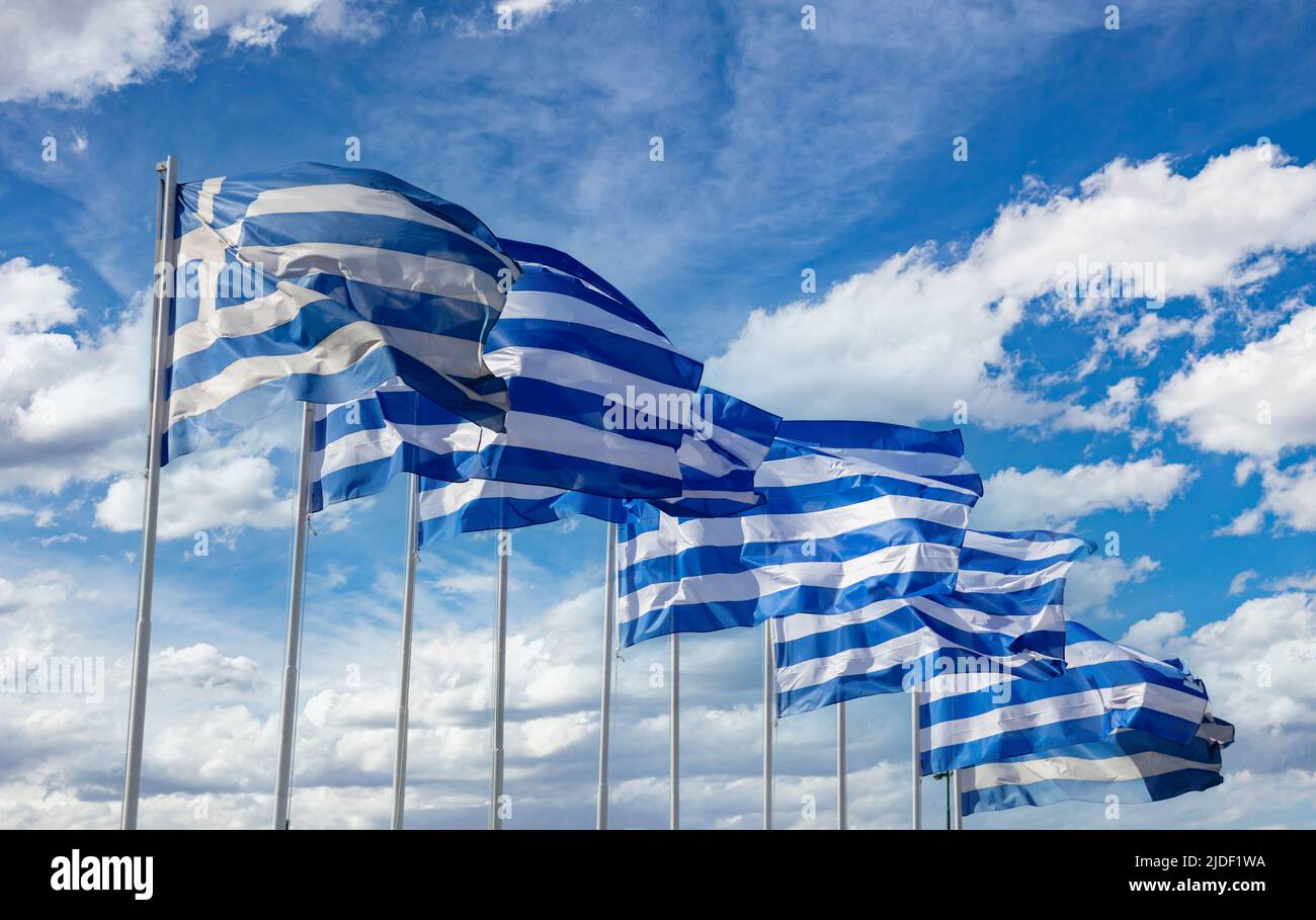 Simbolo di segno della Grecia, cielo blu nuvoloso, giorno di primavera soleggiato ad Atene. Bandiere ufficiali nazionali greche sui flagpoli in fila che ondeggiano nel vento. Foto Stock