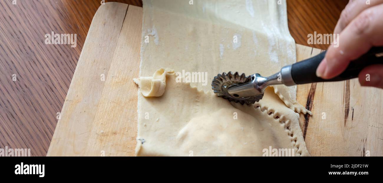 Kalitsounia preparazione tradizionale delle torte cretese. Mano femmina con una ruota di pasta frolla tagliando pasta fatta in casa farcita con formaggio di siero di latte dolce ed erbe, chiudere Foto Stock