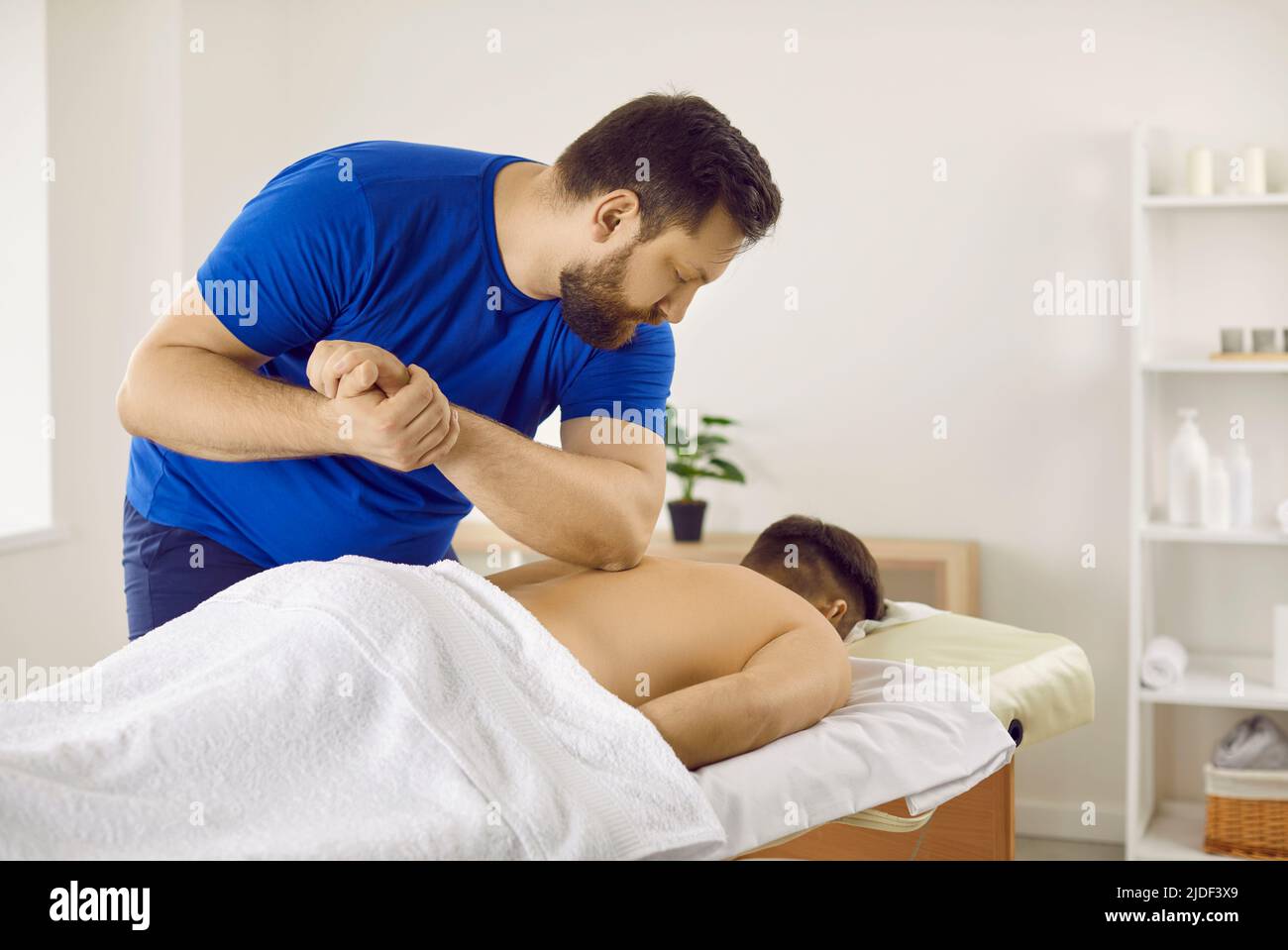 Il massaggiatore professionale maschio preme il gomito sulla schiena del paziente durante la sessione di massaggio. Foto Stock