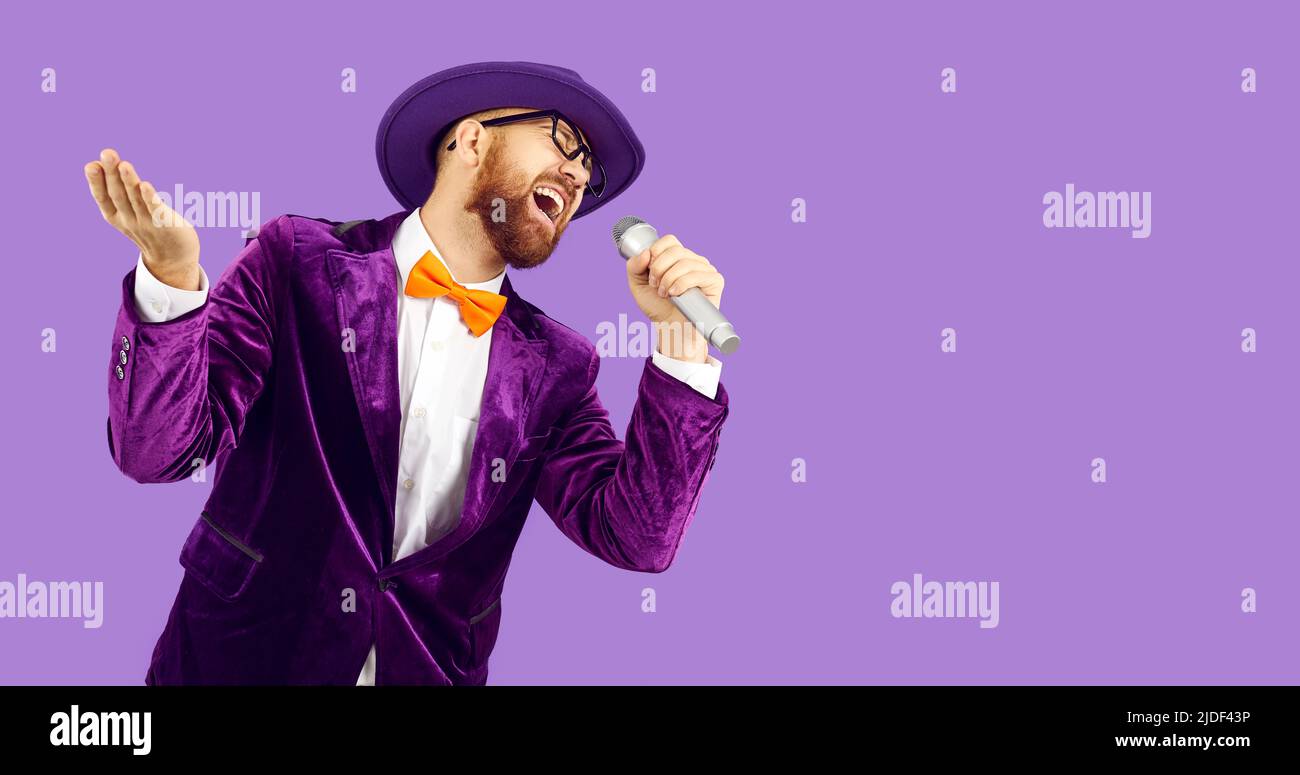 Divertente uomo emozionale che tiene il microfono per karaoke e cantare canzoni di festa su sfondo viola. Foto Stock
