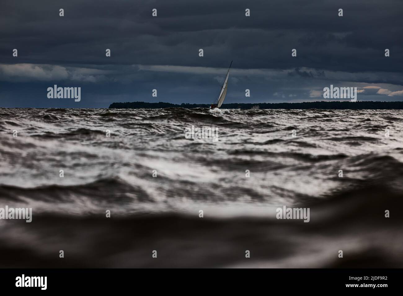 Barca a vela in mare a tempesta, nuvole tempesta cielo arancione, regata vela, riflesso della vela in acqua, bigl onde d'acqua, Foto Stock