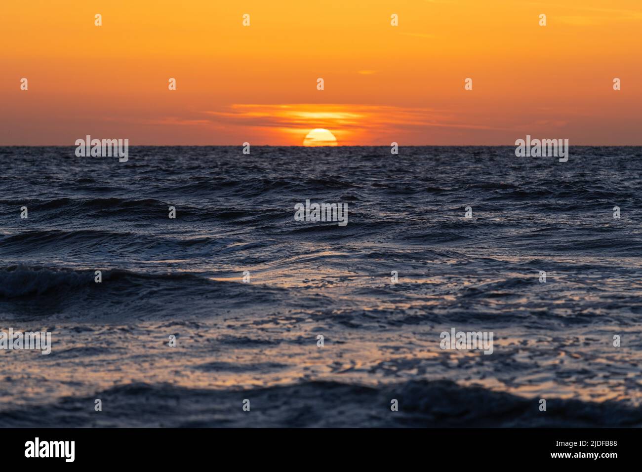 Sole che si staglia sotto l'orizzonte dal Mare del Nord, Belgio. Foto Stock