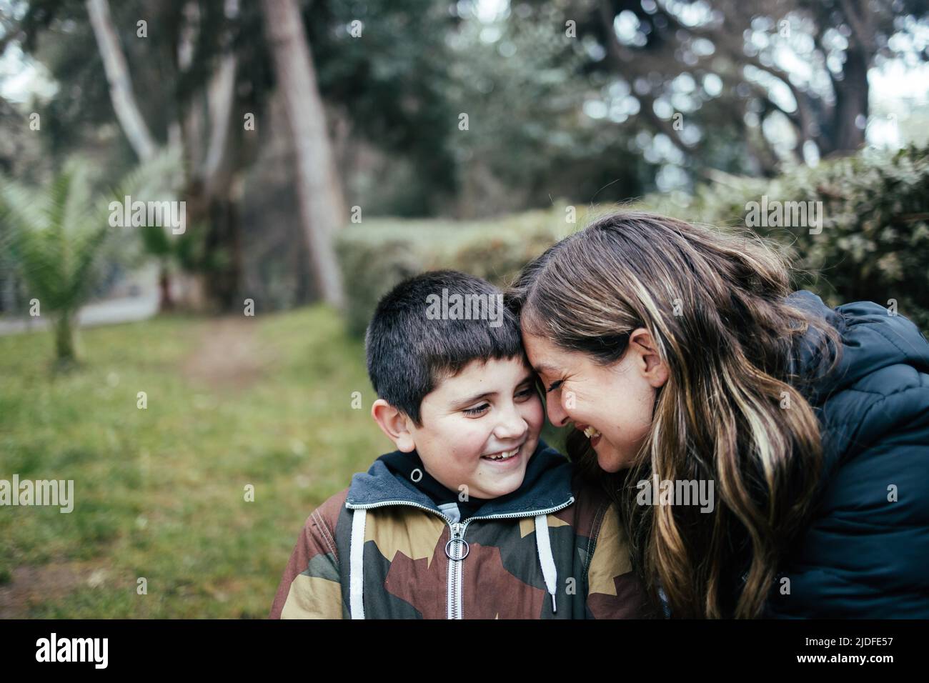 Giovane madre bionda latina che abbraccia e ride con il suo figlio giovane nel parco. Famiglia con un solo genitore Foto Stock