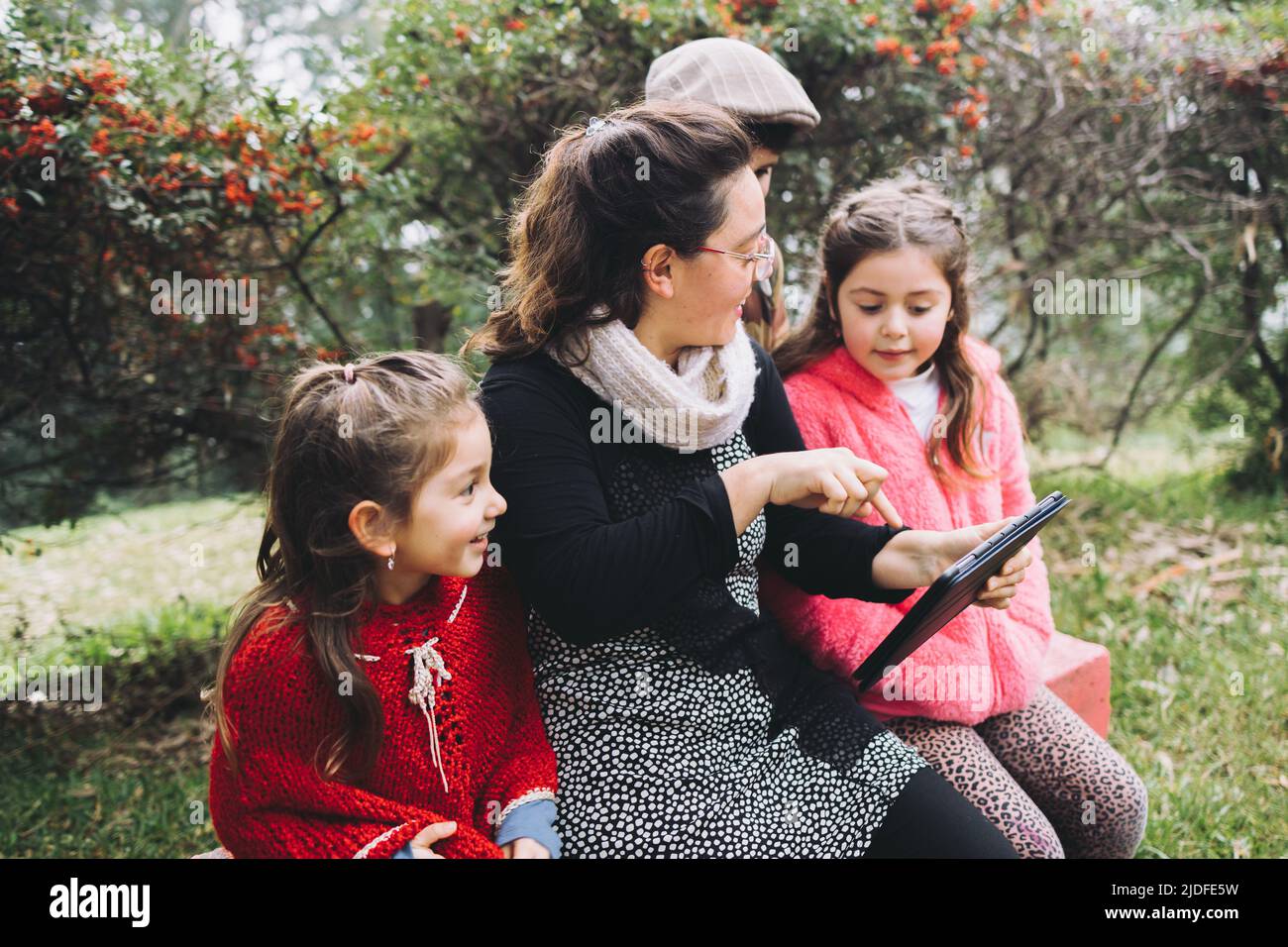 Madre single con suo figlio e le figlie che usano un tablet per guardare un film, nel parco. Famiglia latina singola Foto Stock