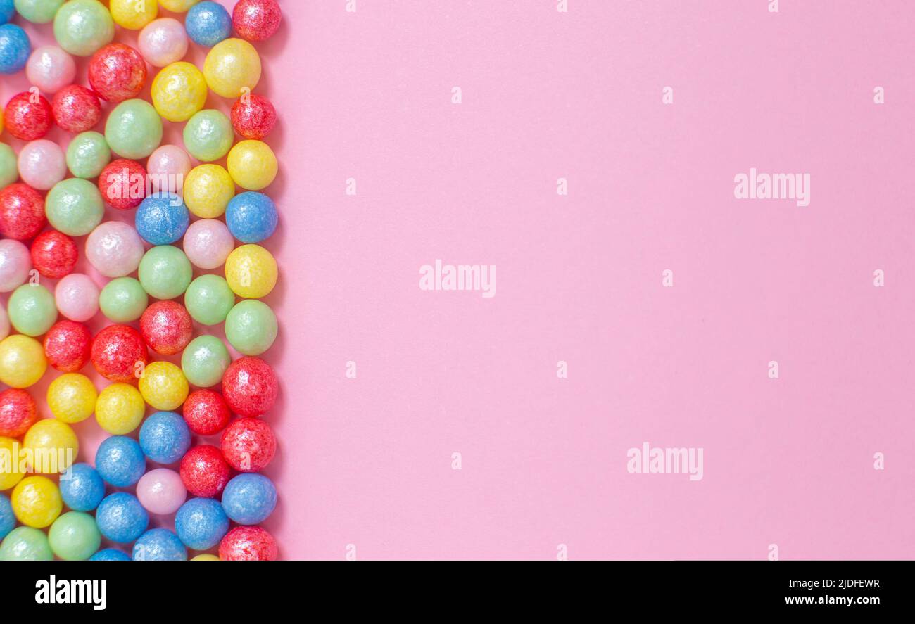 Palline colorate rotonde lucide di condimento zuccherino giacciono a sinistra su sfondo rosa. Foto Stock