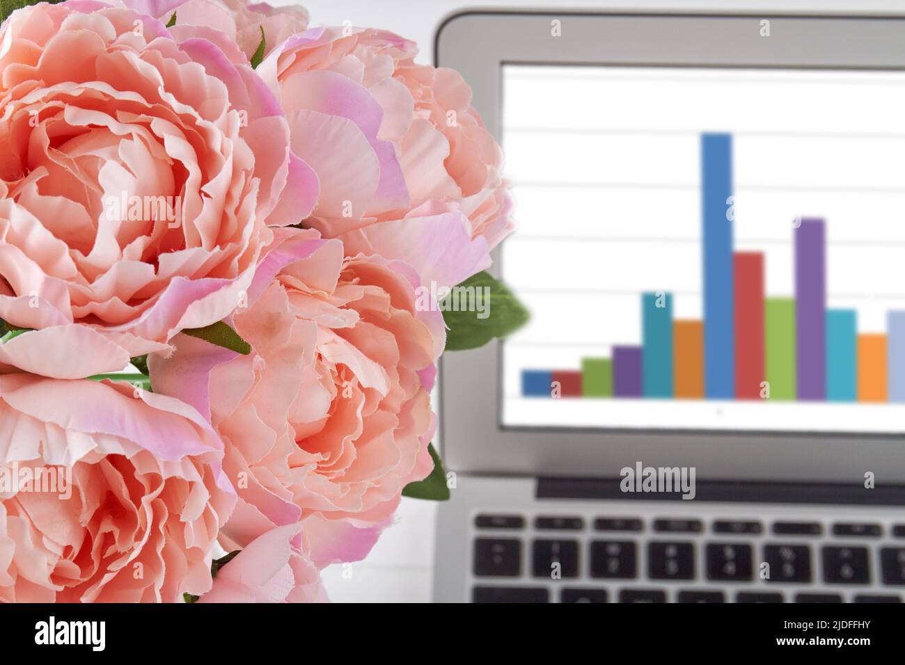 Primo piano peonie rosa e notebook con grafici. Fiori e computer. Foto Stock