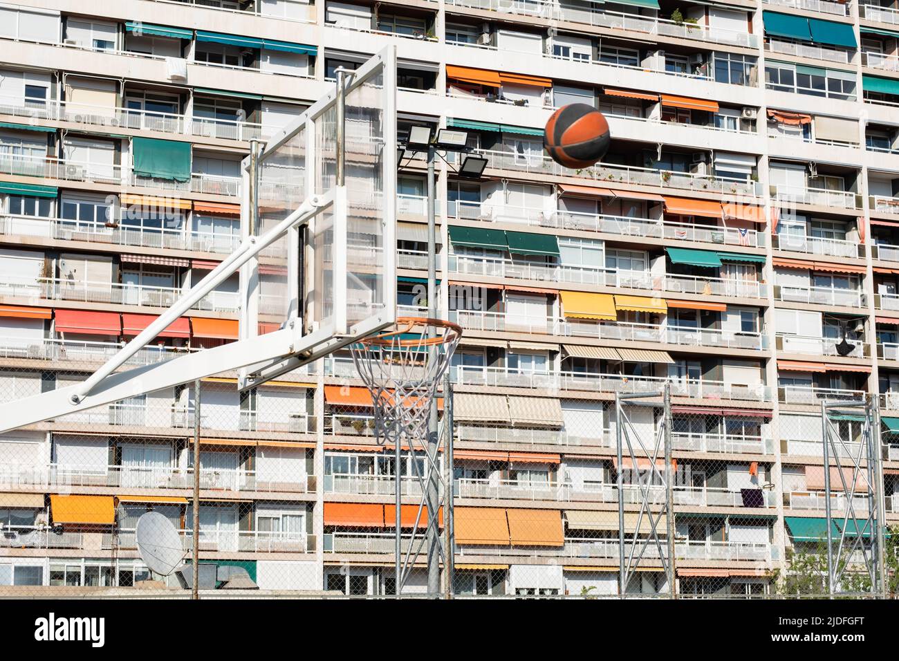 Palla volando verso un cestino con un edificio residenziale sullo sfondo, concetto di sport urbani all'aperto, intrattenimento sportivo in città. Foto Stock