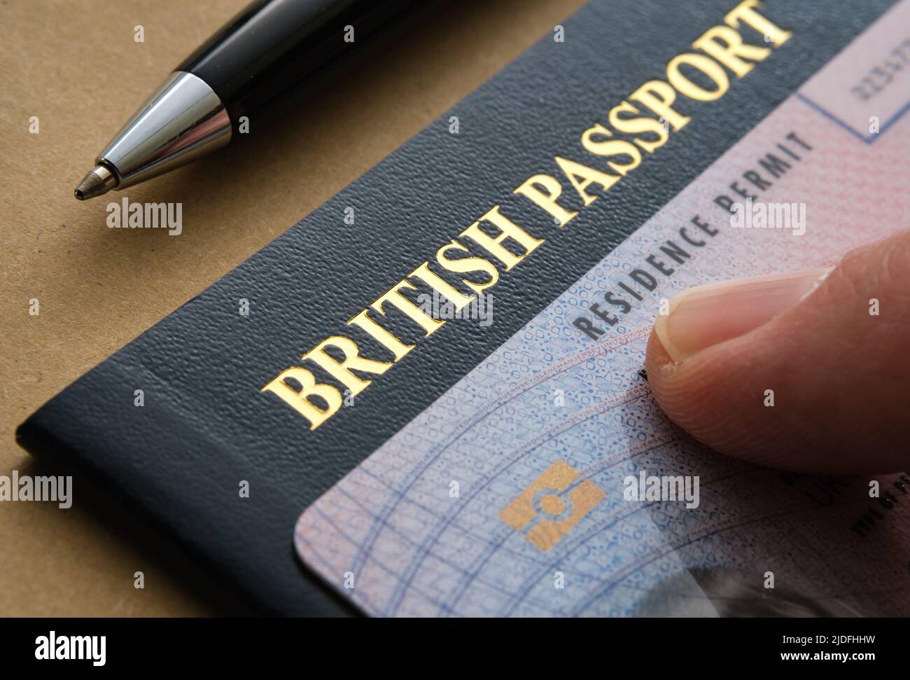 Dito rivolto verso la carta di permesso di soggiorno biometrica (ILR, permesso indefinito per rimanere) posta sopra il passaporto britannico. Concetto di naturalizzazione. Foto Stock