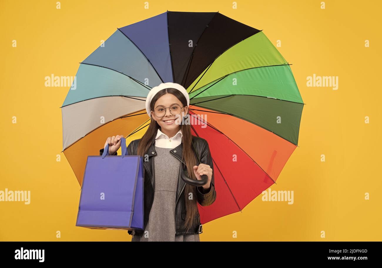 ragazza felice in occhiali tenere shopping bag. vendita stagionale. bambino teen sotto ombrellone colorato. Foto Stock