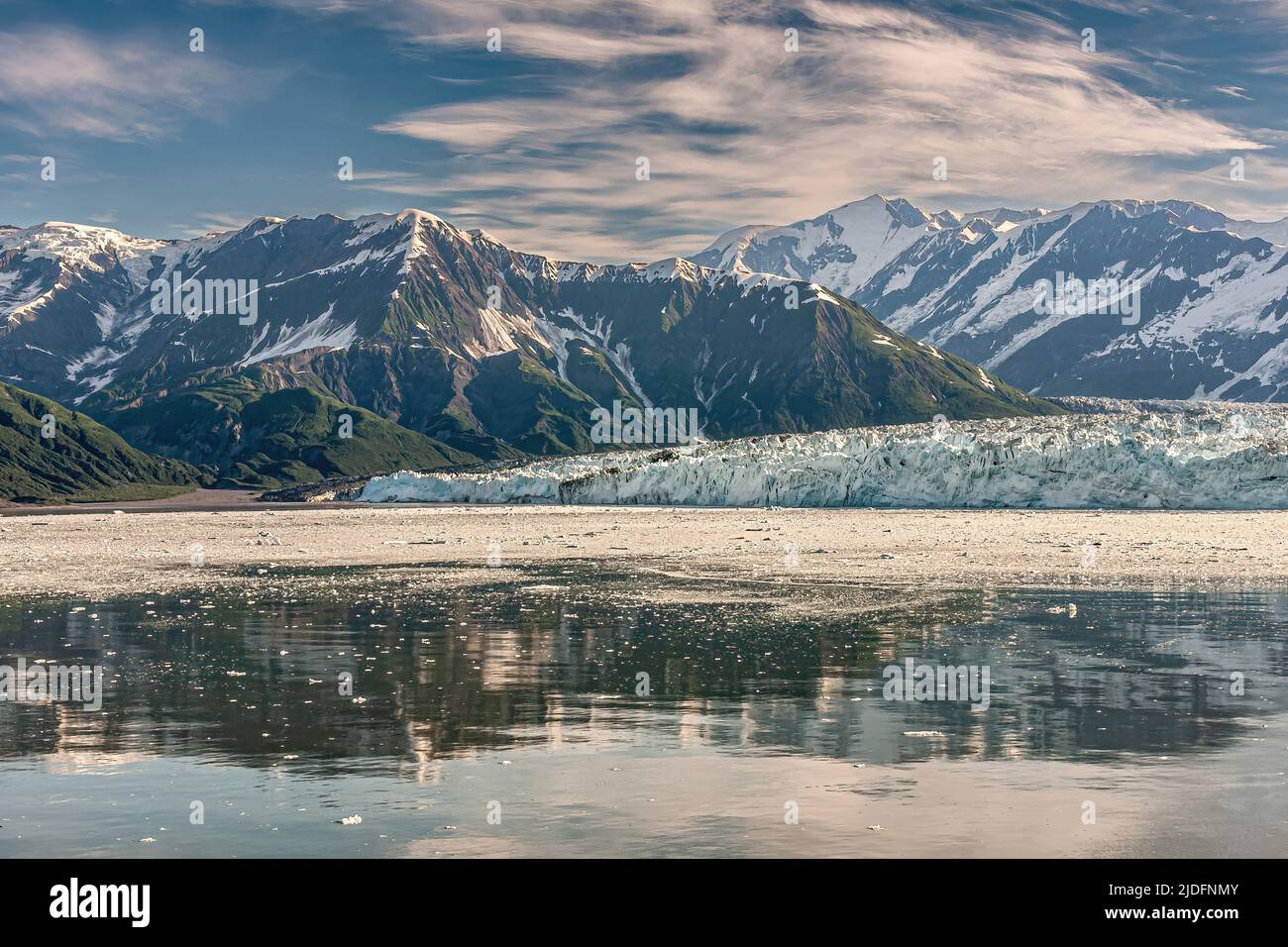 Disincantment Bay, Alaska, USA - 21 luglio 2011: La catena montuosa coperta di neve si riflette in parte nell'acqua dell'oceano di fronte al ghiacciaio Hubbard blu-bianco ic Foto Stock