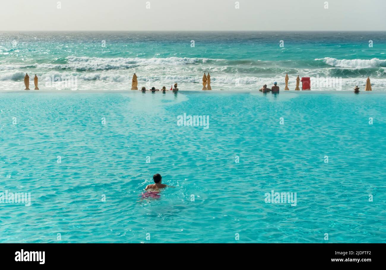 Persone in una piscina a sfioro di fronte al mare Foto Stock