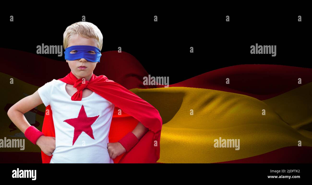 Ragazzo caucasico in costume da supereroe contro la bandiera spagnola ondeggiante con spazio copia su sfondo nero Foto Stock